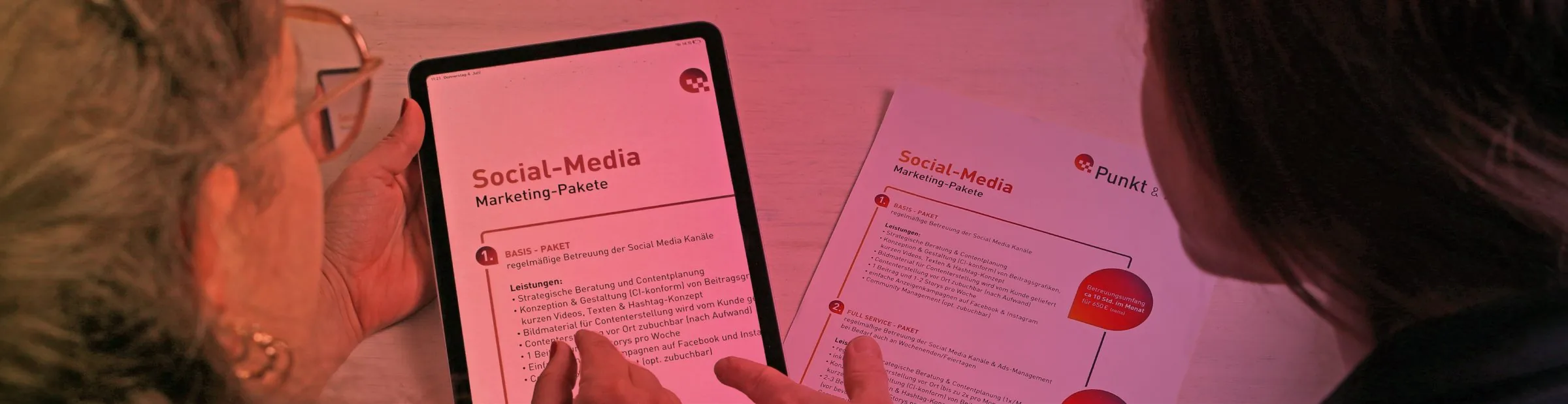 Zwei Personen besprechen einen Social-Media-Redaktionsplan auf einem Tablet